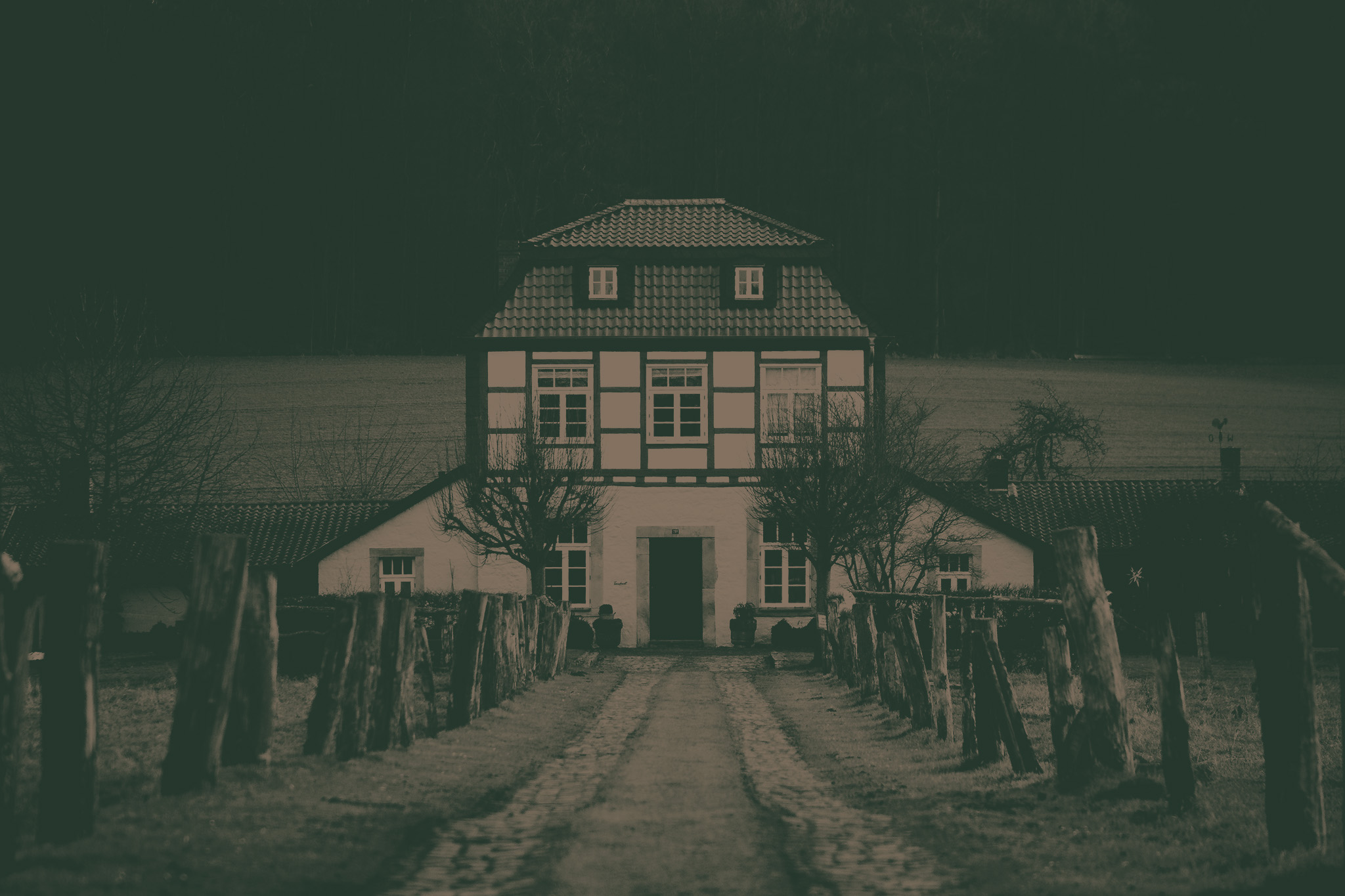 Vertical shot of pathway with wooden post barriers to an old rural house on a gloomy day